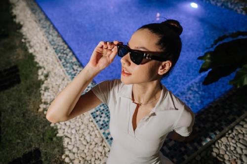 Una donna con gli occhiali da sole seduta accanto alla piscina. di The Courtyard Chiangrai a Chiang Rai