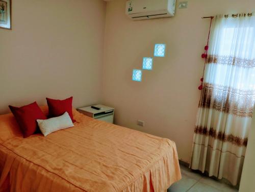 Departamento 2 Complejo Sol de Oeste في سان خوان: غرفة نوم بها سرير مع وسائد حمراء ونافذة