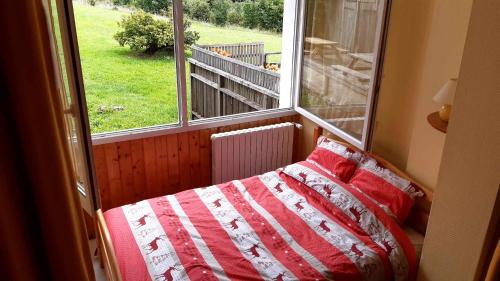 - un lit avec une couverture rouge et blanche devant une fenêtre dans l'établissement Les Angéliques, à Gérardmer