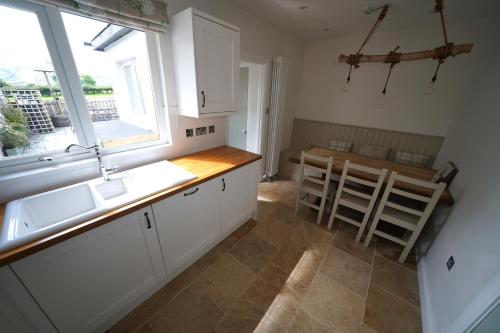 una cucina con armadi bianchi, tavolo e finestra di Gortnagory Cottage Carnlough a Carnlough