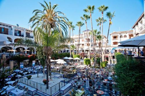 un patio al aire libre con mesas, sillas y palmeras en Apartment VillaMartin Plaza - The Loft, en Orihuela Costa