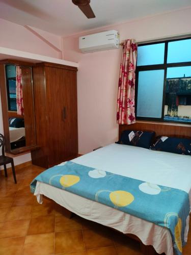 a bedroom with a large bed with a blue comforter and a window at Villa Cleto Guest House in Panaji