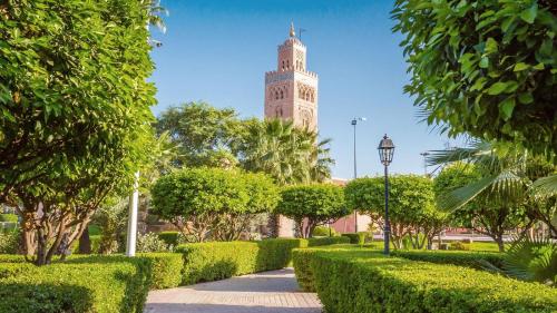 une tour d'horloge au milieu d'un parc avec des buissons dans l'établissement Dar Baddi, à Marrakech