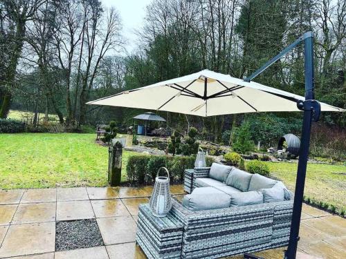 a patio with a couch and an umbrella at Bonshaw Grange-Riverside Country Retreat, & HotTub in Lockerbie