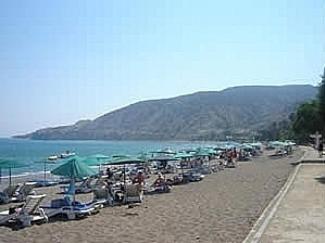 a beach with a bunch of chairs and umbrellas at Yialos Apartments in Pissouri