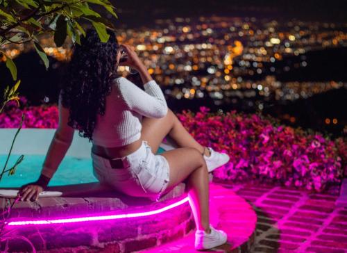 a woman sitting next to a pool with pink lights at Romero Glamping y Cabañas in Cali