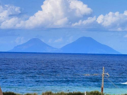 een uitzicht op de oceaan met twee bergen in de verte bij "Appartamento del Mare Gliaca" con vista Isole Eolie,ampia terrazza,wifi e parcheggio gratuito in Piraino