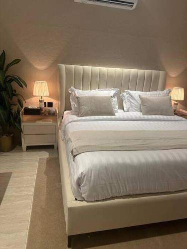 a white bed with white pillows and a table with a lamp at Three Bedroom furnished apartment in north Riyadh - شقه 3 غرف مميزه ومتكامله في شمال الرياض مع مرافق فريده in Riyadh