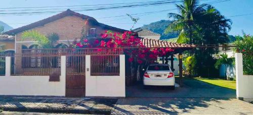 een auto geparkeerd voor een huis met roze bloemen bij Casa em mangaratiba in Mangaratiba