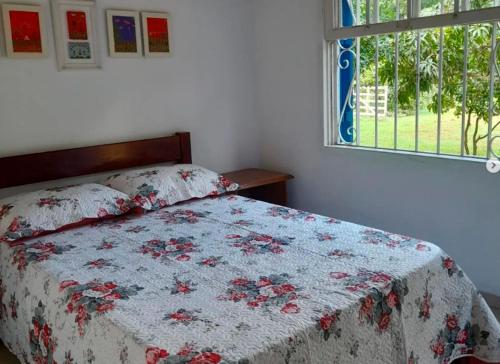 a bedroom with a bed with a floral bedspread and a window at O Casarão in Passa Quatro
