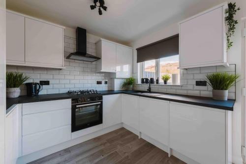 La cuisine est équipée de placards blancs et d'un four avec plaques de cuisson. dans l'établissement SleepLuxury ApartHOUSE, à Glasgow