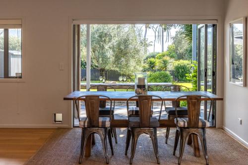 a dining room with a table and chairs and a large window at Paradise on Palm - Stay Waiheke in Palm Beach