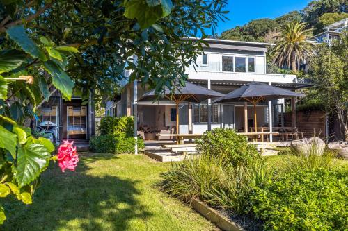 a house with tables and umbrellas in a yard at Paradise on Palm - Stay Waiheke in Palm Beach