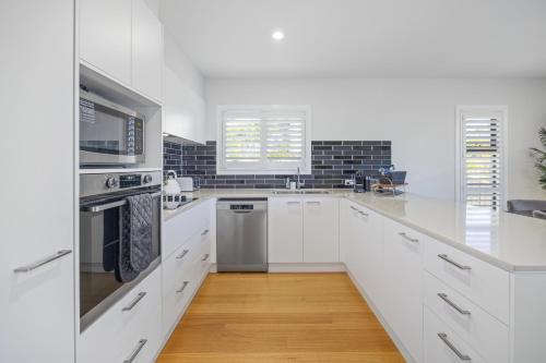 a white kitchen with white cabinets and a microwave at Port Macquarie Ocean Escape in Port Macquarie