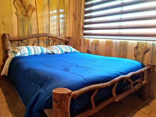 a wooden bed with blue sheets in a room with a window at Refugio Wanglen Cabañas y Tinajas hidromasaje in Lago Ranco