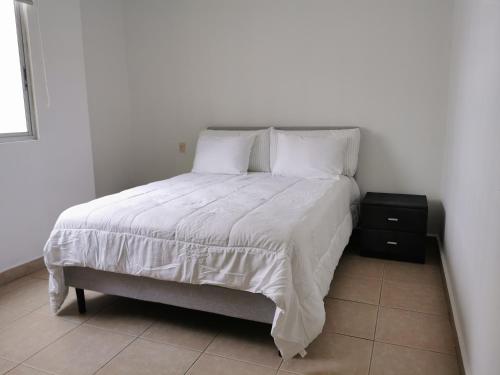 ein Bett mit weißer Bettwäsche und Kissen sowie einem Nachttisch in der Unterkunft Habitación privada en zona exclusiva in Panama-Stadt