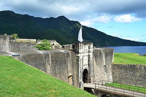Un antiguo castillo con una torre y un cuerpo de agua. en Logement dans un lieu calme et verdoyant à proximité de tout avec Jacuzzi!!!, en Basse-Terre
