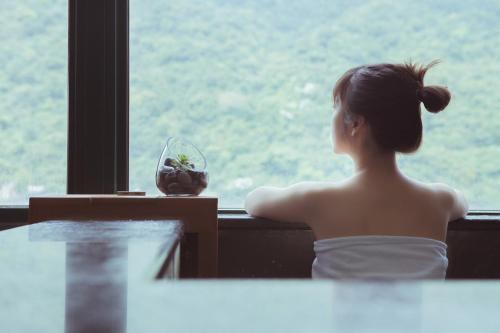 Una donna con un vestito bianco che guarda fuori da una finestra di Muen Hot Spring Hotel a Jiaoxi