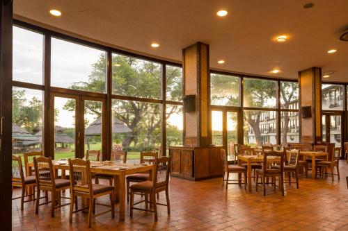a dining room with tables and chairs and large windows at Hwange Safari Lodge in Dete