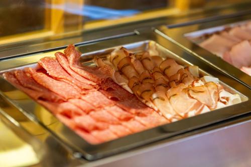 a display case with a tray of bacon and other food at Hotel Bergland in Sillian