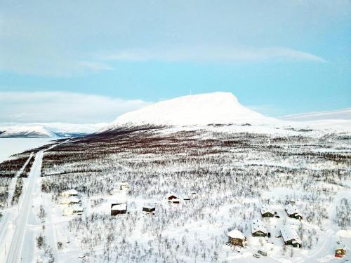 a village in a snow covered field with a snow covered mountain at Lapland Hotels Kilpis in Kilpisjärvi