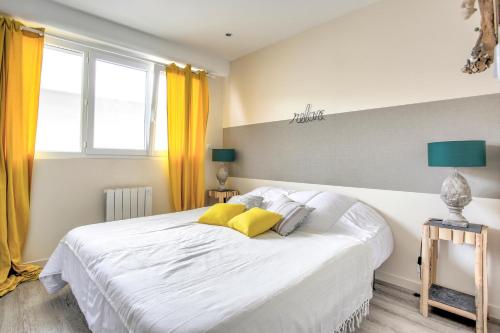 Un dormitorio con una gran cama blanca con almohadas amarillas. en Val Détente - Appartement à proximité immédiate de la plage, en Pléneuf-Val-André