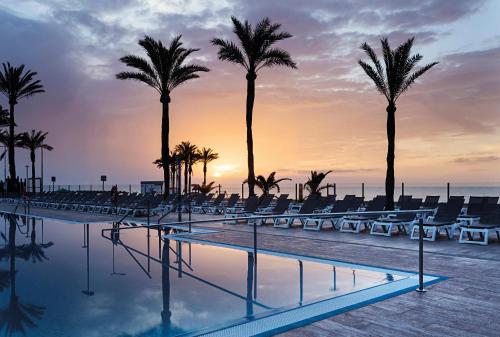 a pool with palm trees and chairs at sunset at Hotel Best Sabinal in Roquetas de Mar