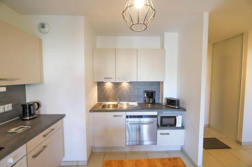 une cuisine avec des armoires blanches, un évier et un micro-ondes dans l'établissement Le Discret T2 aux portes de la vieille ville, à Annecy