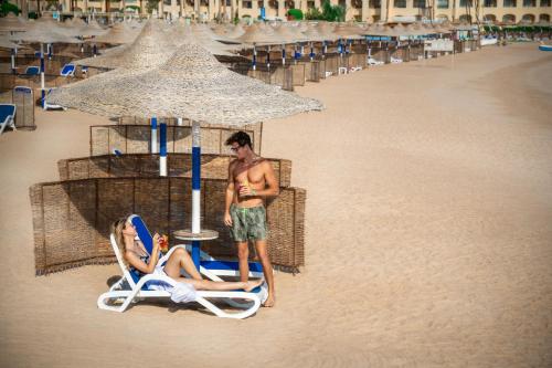 a man and a woman sitting in a chair on the beach at Cleopatra Luxury Resort Makadi Bay in Hurghada