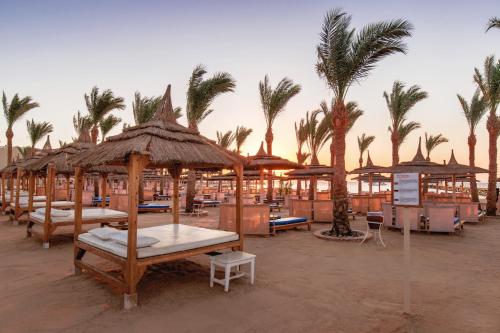a beach with tables and umbrellas and palm trees at Pickalbatros Palace - Aqua Park Hurghada in Hurghada