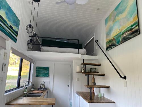 uma pequena casa com uma cama alta e um lavatório em Little Pardalote Tiny Home Bruny Island em Alonnah