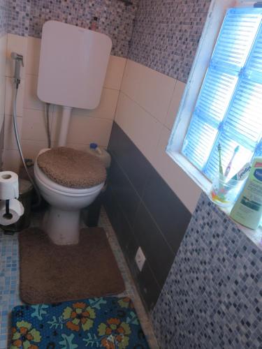 baño con aseo, ventana y alfombra en Casa de Nômades Digitais en Mindelo