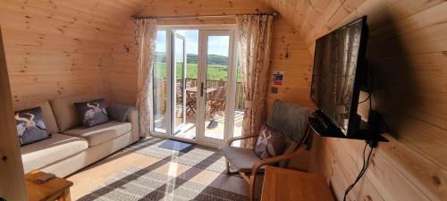 a living room with a couch and a television in a cabin at Beautiful Glamping Pod with Central Heating, Hot Tub, Garden, Balcony & views - close to Cairnryan - The Herons Nest by GBG in Glenluce