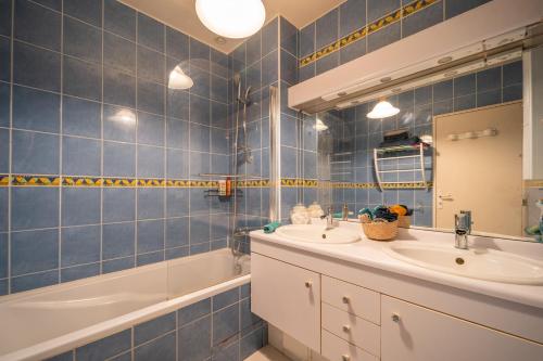 La salle de bains est pourvue de carrelage bleu, d'un lavabo et d'une baignoire. dans l'établissement Les Volets Bleus, à Rungis