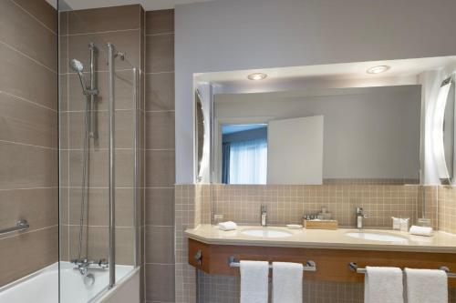 a bathroom with two sinks and a shower and a mirror at Delta Hotels by Marriott Waltham Abbey in Waltham Abbey