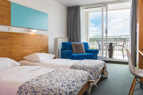 um quarto de hotel com duas camas e uma cadeira azul em Hotel Oleander - Oleander Resort em Strunjan