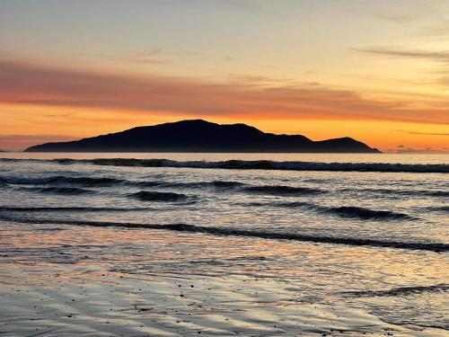 a sunset over a beach with a mountain in the background at The Beachsider - Te Horo Beach Holiday Home in Te Horo