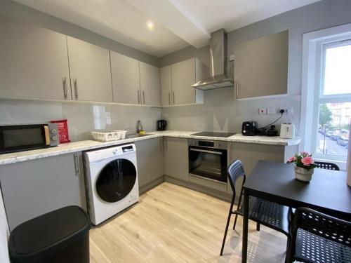 a kitchen with a dishwasher and a table with chairs at Holloway Suites - Next To Emirates Stadium - Private Bathroom - Shared Kitchen in London