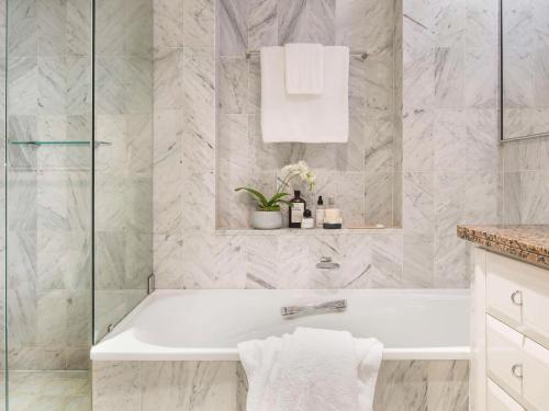 uma banheira branca na casa de banho com azulejos de mármore em The Sebel Quay West Suites Sydney em Sidney
