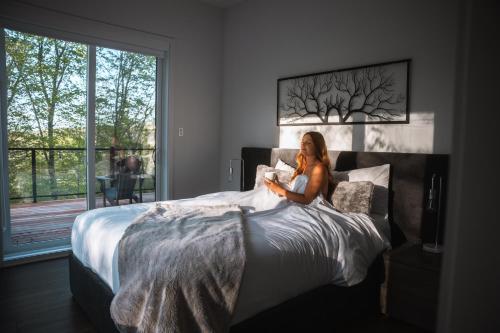 a woman sitting on a bed reading a book at Bellaria with SPA near Mercier Lake in La Conception