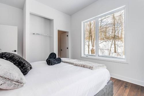 a white bedroom with a bed and a window at Bellaria with SPA near Mercier Lake in La Conception