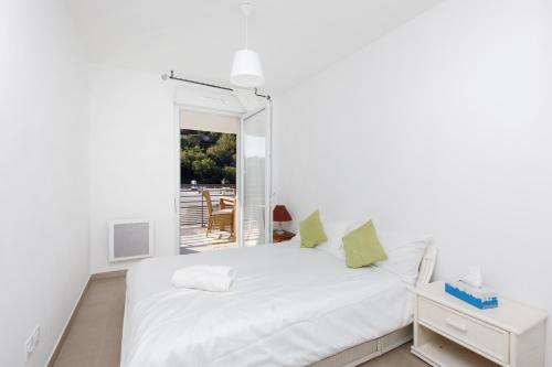 a white bedroom with a white bed with green pillows at Lovely 2 bedroom condo with pool in Vallauris