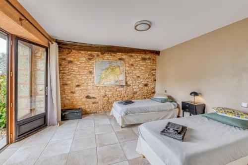 a bedroom with two beds and a brick wall at Gîte lOragée Les Farguettes in Cadouin