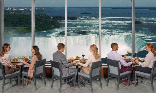 a group of people sitting at tables eating food in front of a waterfall at Embassy Suites by Hilton Niagara Falls/ Fallsview in Niagara Falls