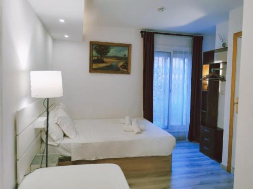 a white bedroom with a bed and a lamp at Barcelona CoronaHostal in Badalona