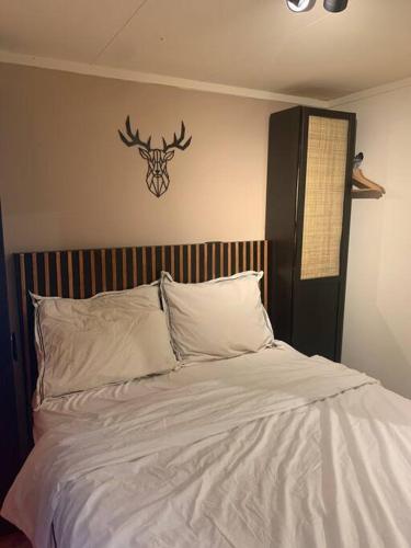 łóżko z białą pościelą i głową jelenia na ścianie w obiekcie Veluws BOHO huis in de natuur w mieście Putten