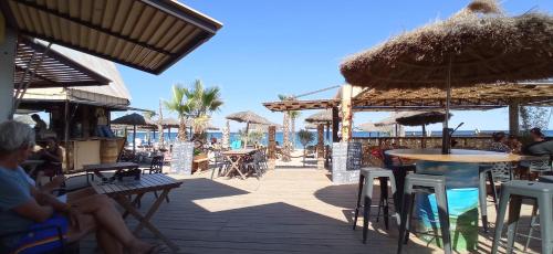 un patio con mesas y sombrillas en la playa en HappyMobilhome Argelès-sur-mer -plage à 500m- Camping 4 étoiles Del Mar, en Argelès-sur-Mer