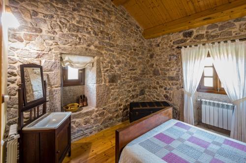 1 dormitorio con cama y pared de piedra en Casa Rural A Avoa María, en Campo Lameiro