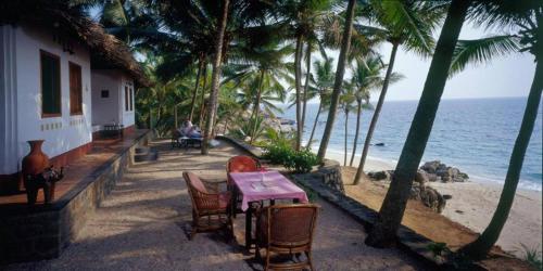 einen Tisch und Stühle neben einem Strand mit Palmen in der Unterkunft Karikkathi Beach House in Thiruvananthapuram