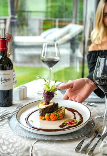 a plate of food on a table with a glass of wine at Hotel Fanes in Selva di Val Gardena